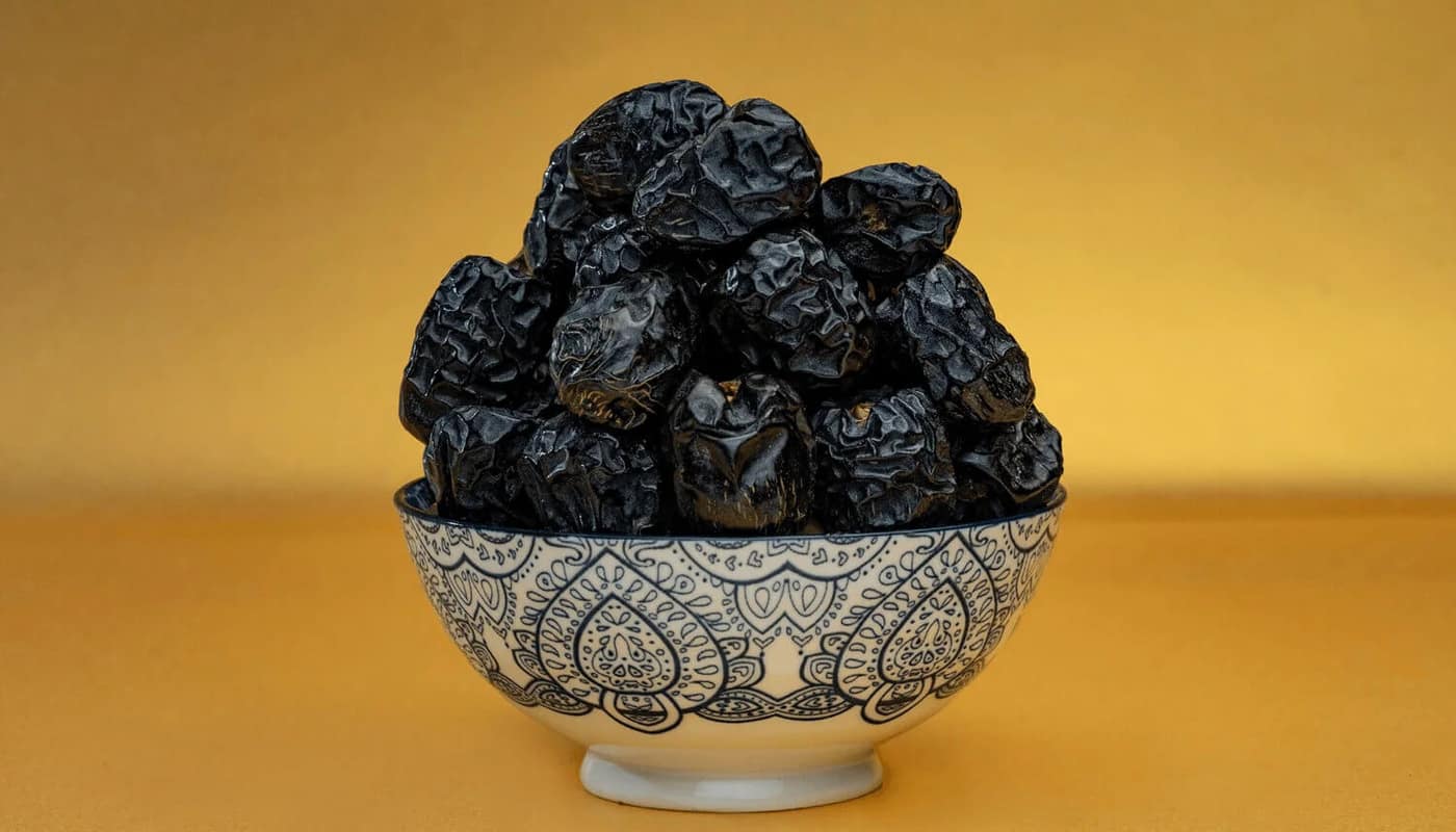 Ajwa dates heaped in a patterned bowl against a warm ochre ground